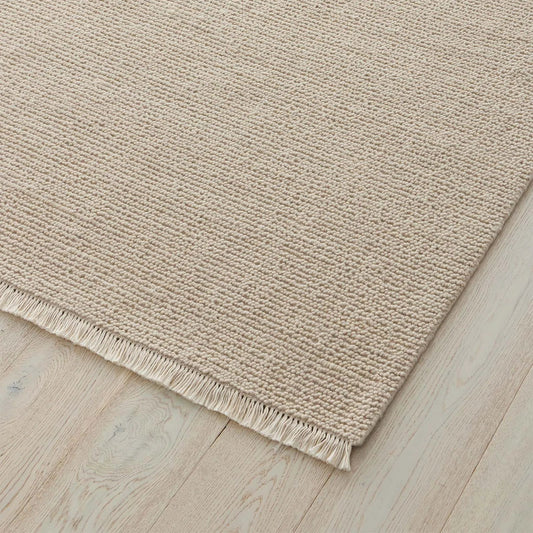 Beige rug with a textured pattern and fringe on a wooden floor. 2x3 3x4. 100% NZ wool