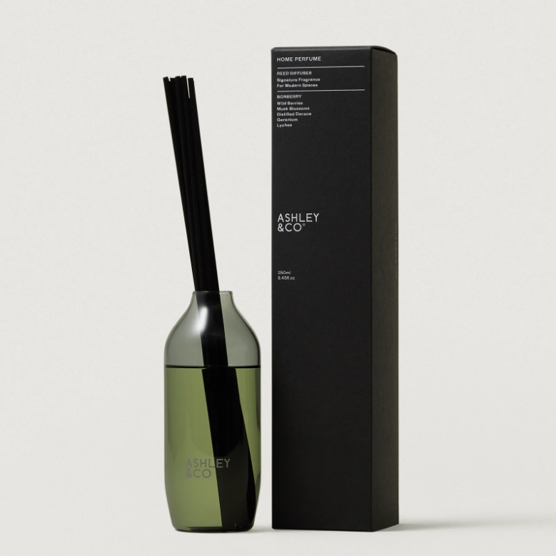 ASHLEY & CO reed diffuser bottle with black reeds next to its black packaging box on a light gray background.