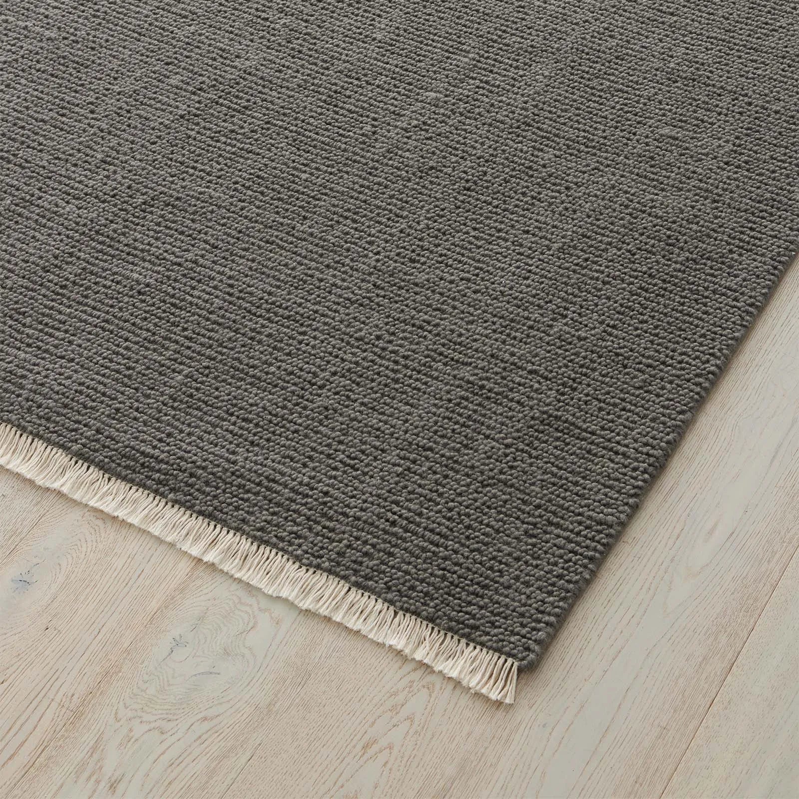 Grey rug with a textured pattern and fringe on a wooden floor. 2x3 3x4. 100% NZ wool