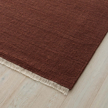 Earthy red rug with a textured pattern and fringe on a wooden floor. 2x3 3x4. 100% NZ wool