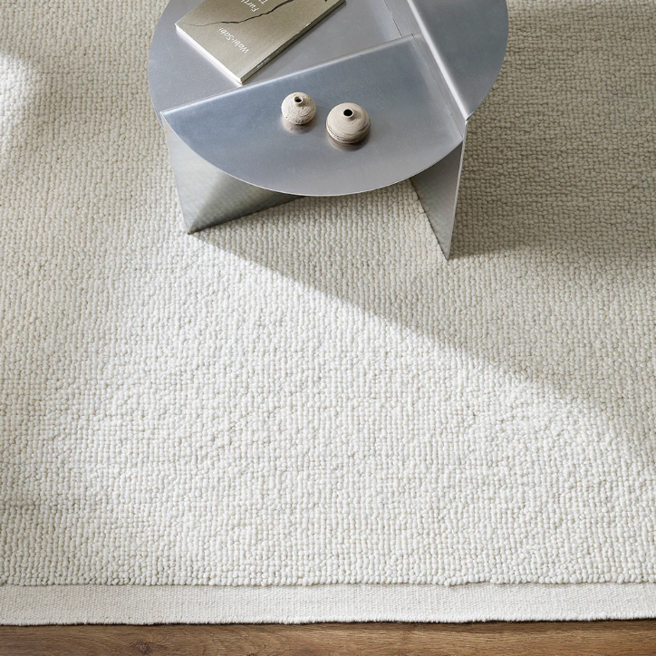 Beige rug on a wooden floor with a small round table in the corner. 100% NZ Wool