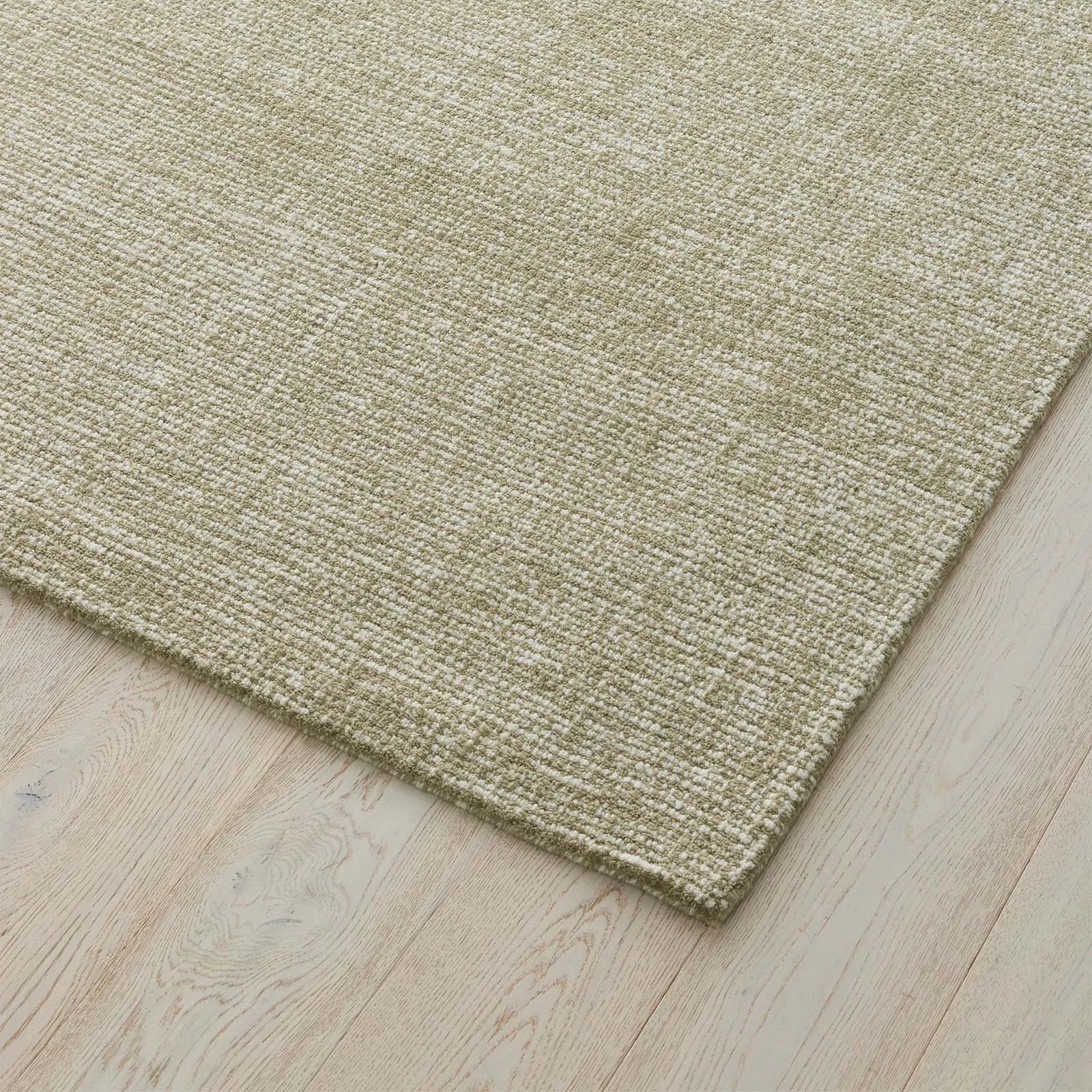 Close-up of a textured green rug on a wooden floor. 2x3. 100% wool rug