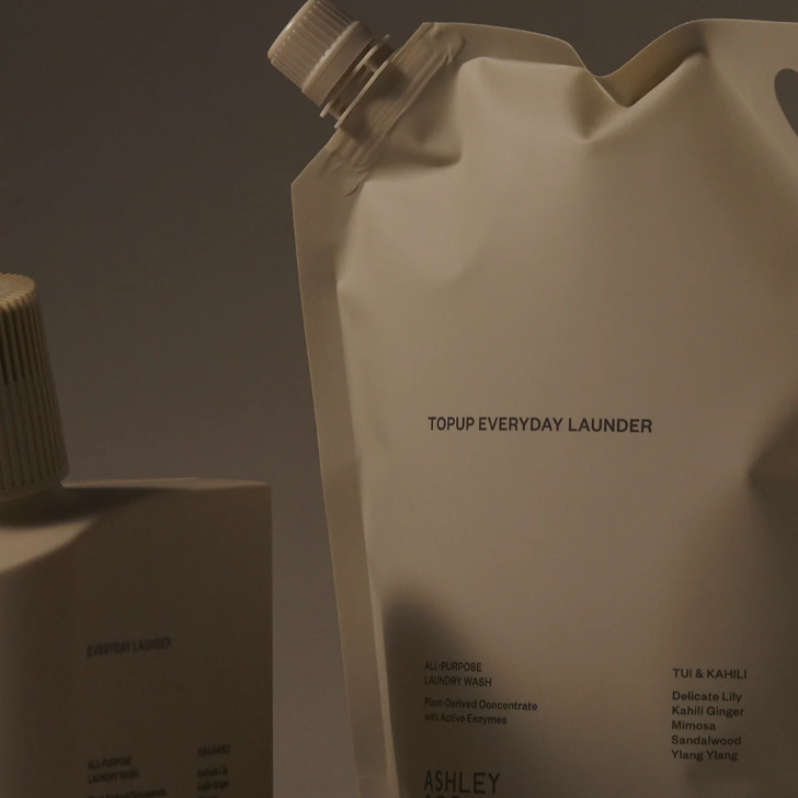 Ashley Topup Everyday Launder refill pouch and bottle in a matching warm off-white color, photographed against a dark gray studio background.